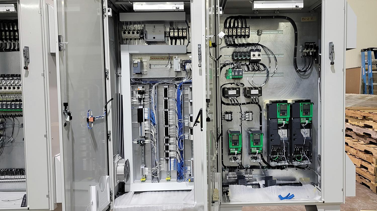 Two large control enclosures with doors open on the shop floor